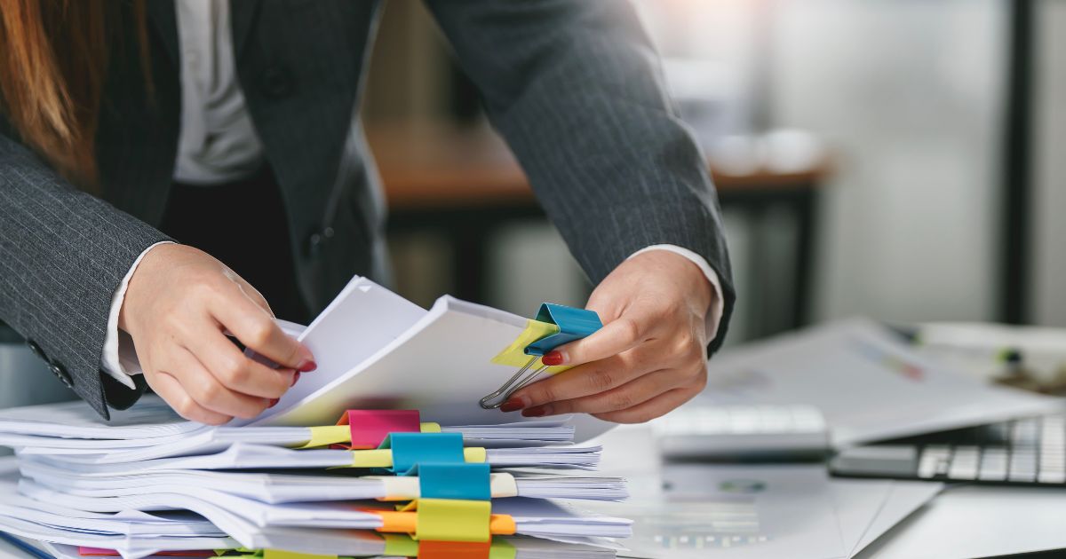 femme qui trie les fiches clients à la main au lieu d'utiliser un outil en ligne qui facilite sa gestion